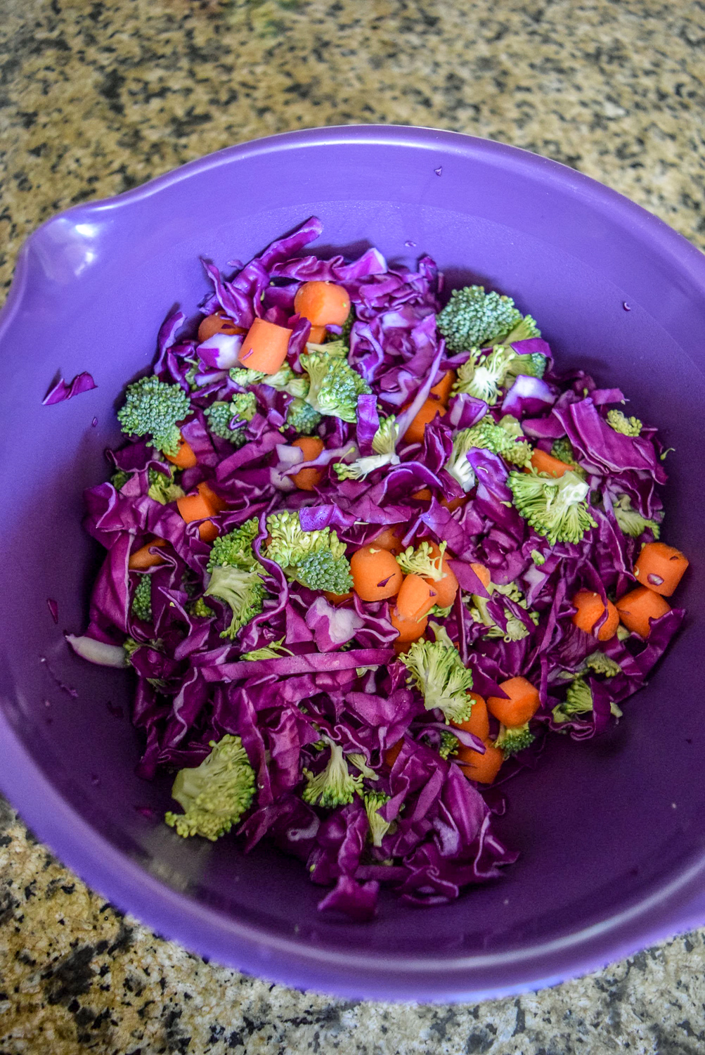Mixed ingredients of red cabbage, broccoli, and carrots in bowl for Sunshine Spicy Mustard Tahini Cruciferous Slaw