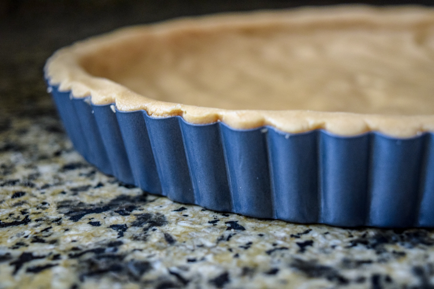 Shortbread dough pressed into tart pan from side up close