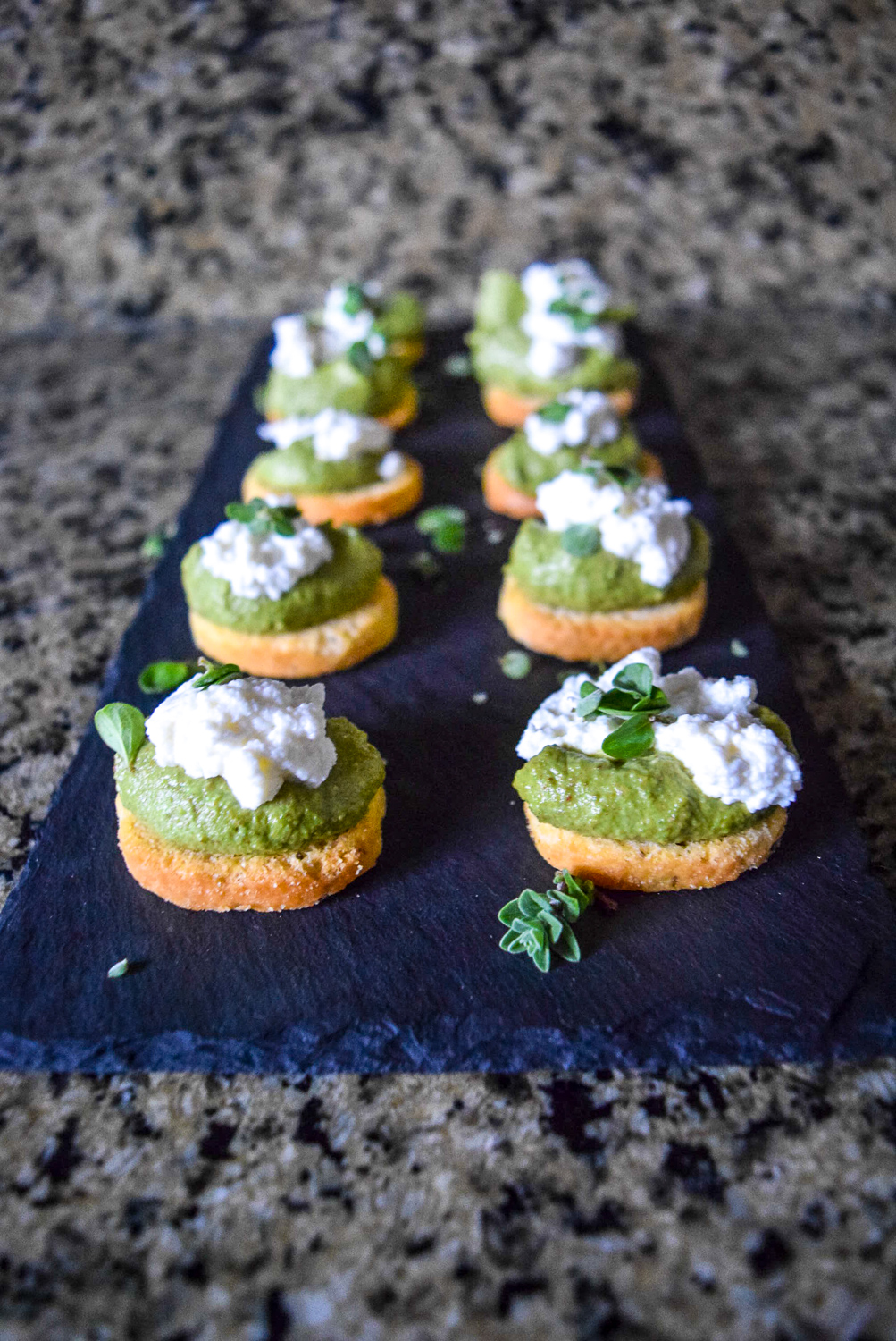 Marjoram Pea Pesto Crostini with Fresh Ricotta on slate cheeseboard from front