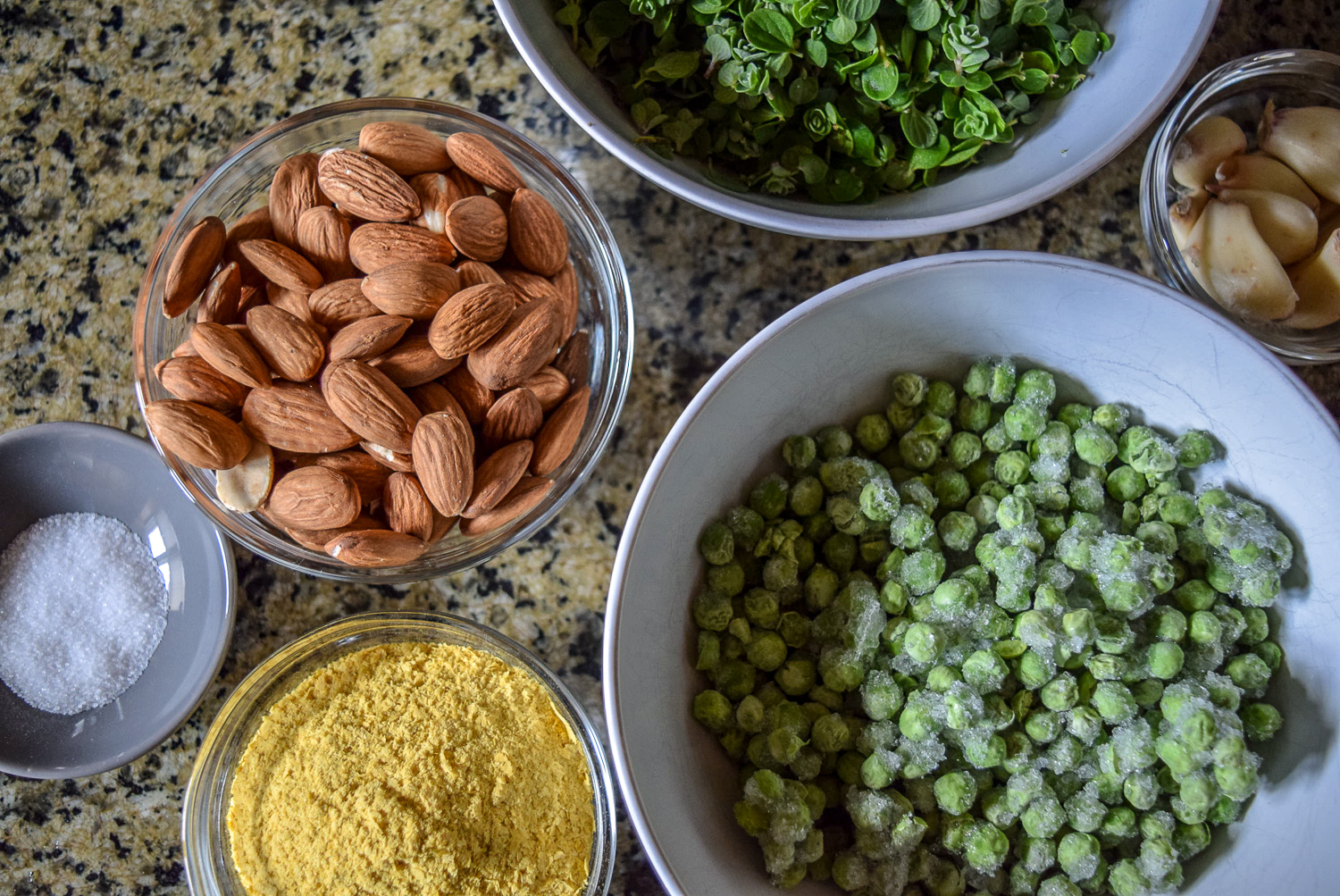 Ingredients for Vegan Marjoram Pea Pesto from top, including homegrown freshly-picked destemmed marjoram herb, frozen peas, almonds, garlic cloves, salt, and nutritional yeast