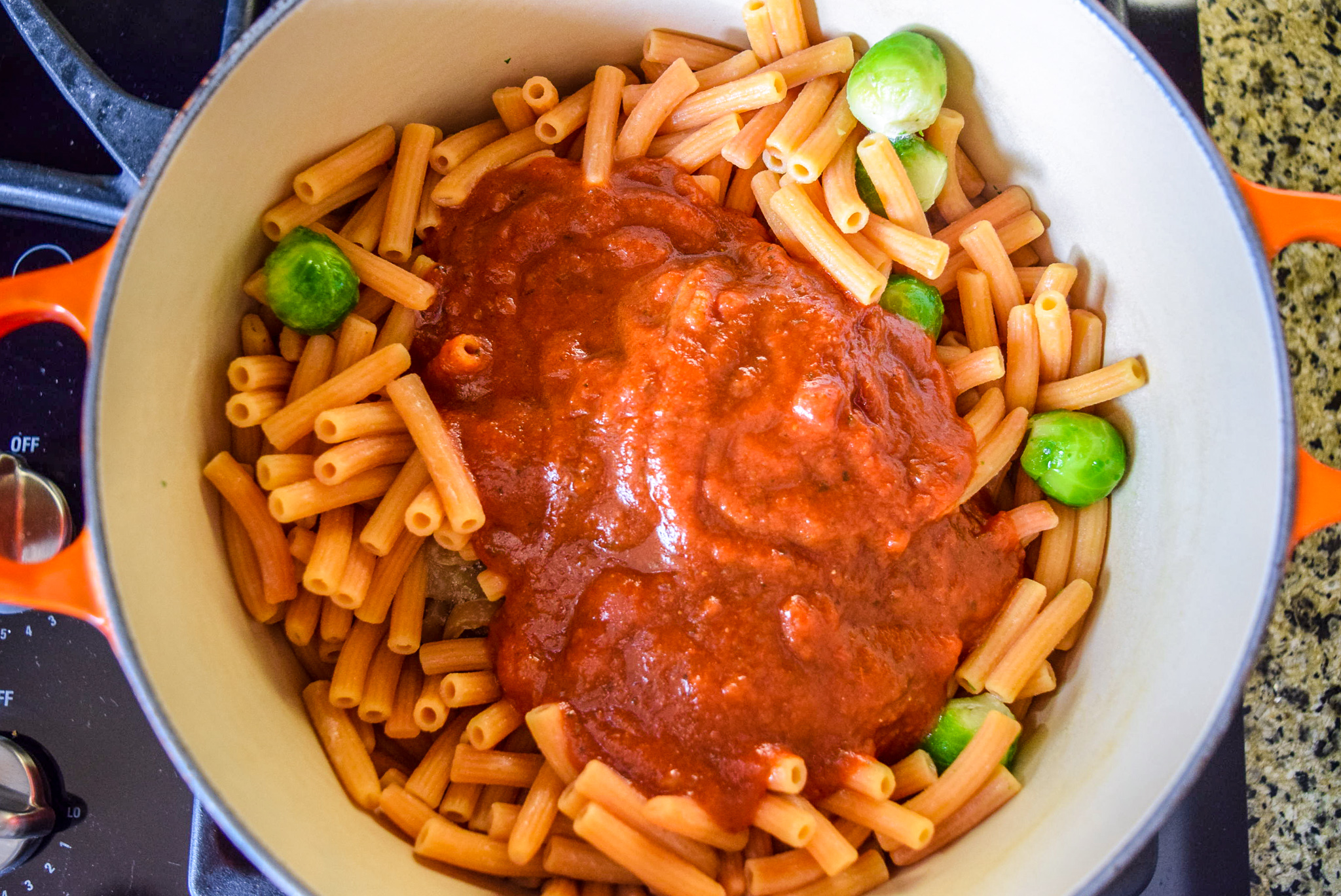Cooked and strained Trader Giotto’s Organic Red Lentil Sedanini Pasta in Flame Le Creuset Dutch Oven with marinara sauce, brussel sprouts, and caramelized onions