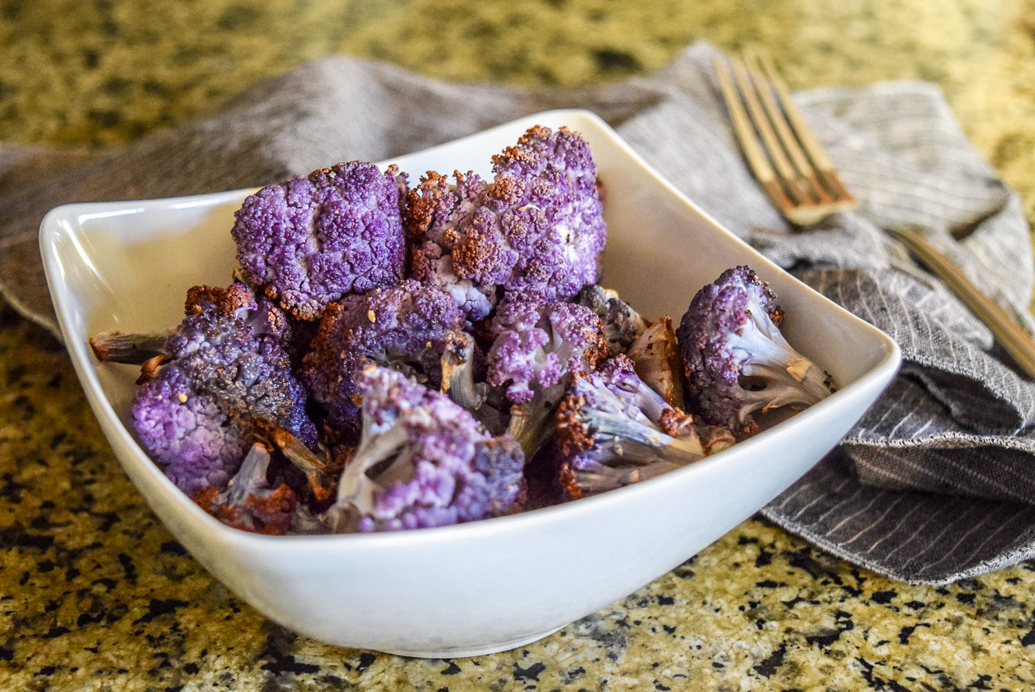 Finished roasted purple cauliflower florets from side angle with fork in background