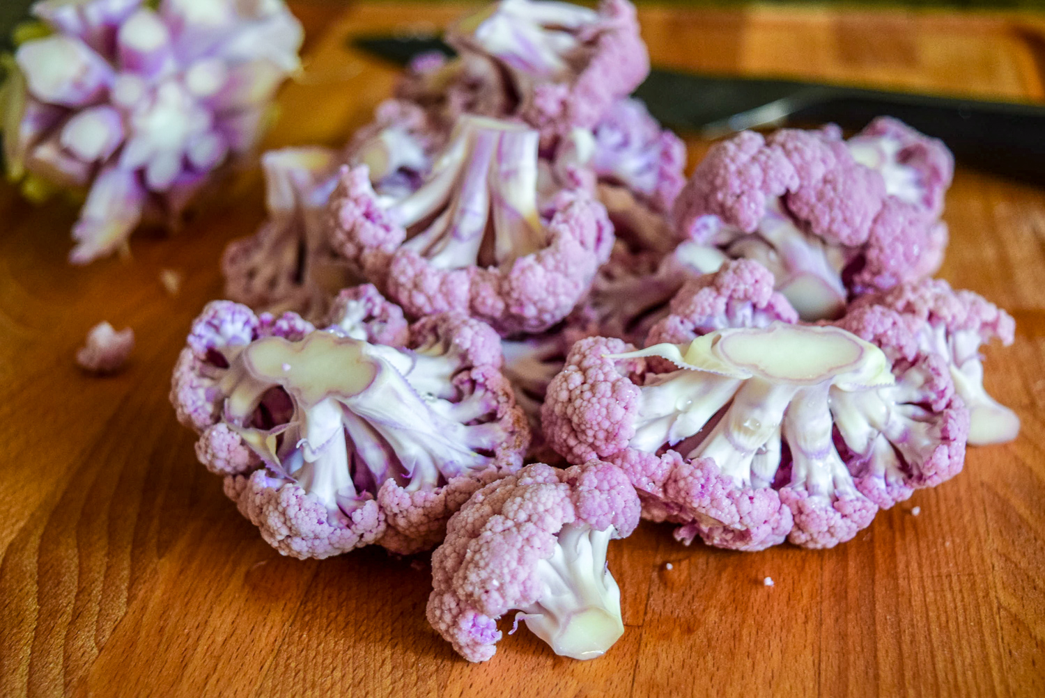 Raw purple cauliflower florets on cuttingboard with stem and knife in background