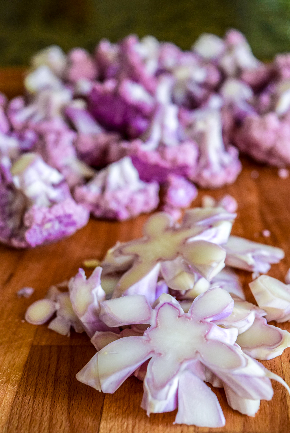 Raw purple cauliflower cut up stem pieces on cutting board with florets in background