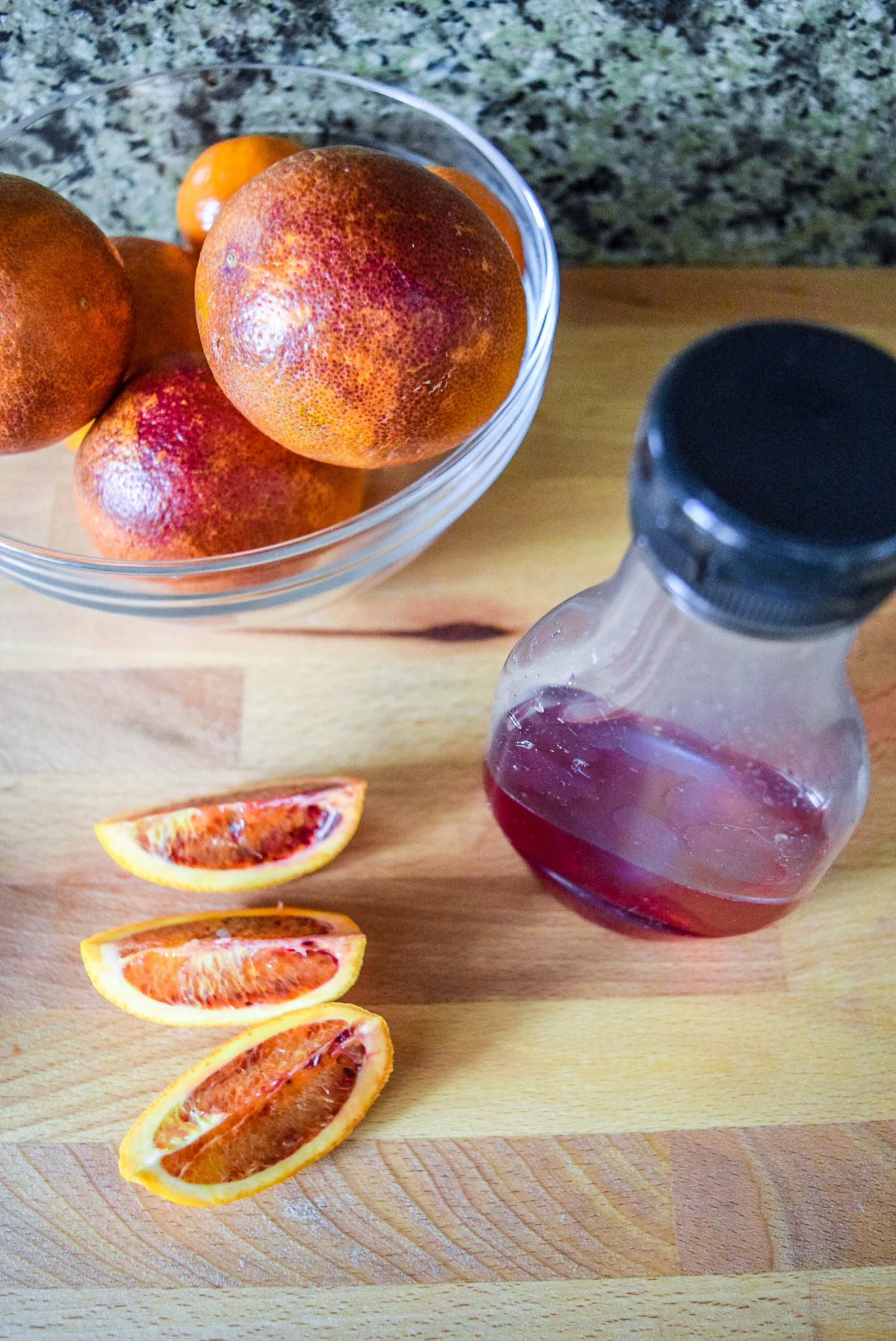 Finished blood orange syrup in bottle with sliced blood oranges from front