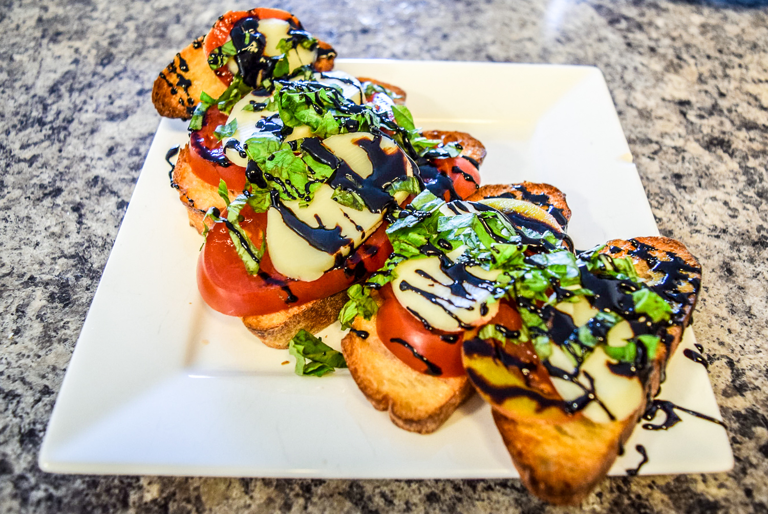 Finished caprese bruschetta with heirloom tomato, fresh basil, homemade mozzerella, and balsamic reduction from front