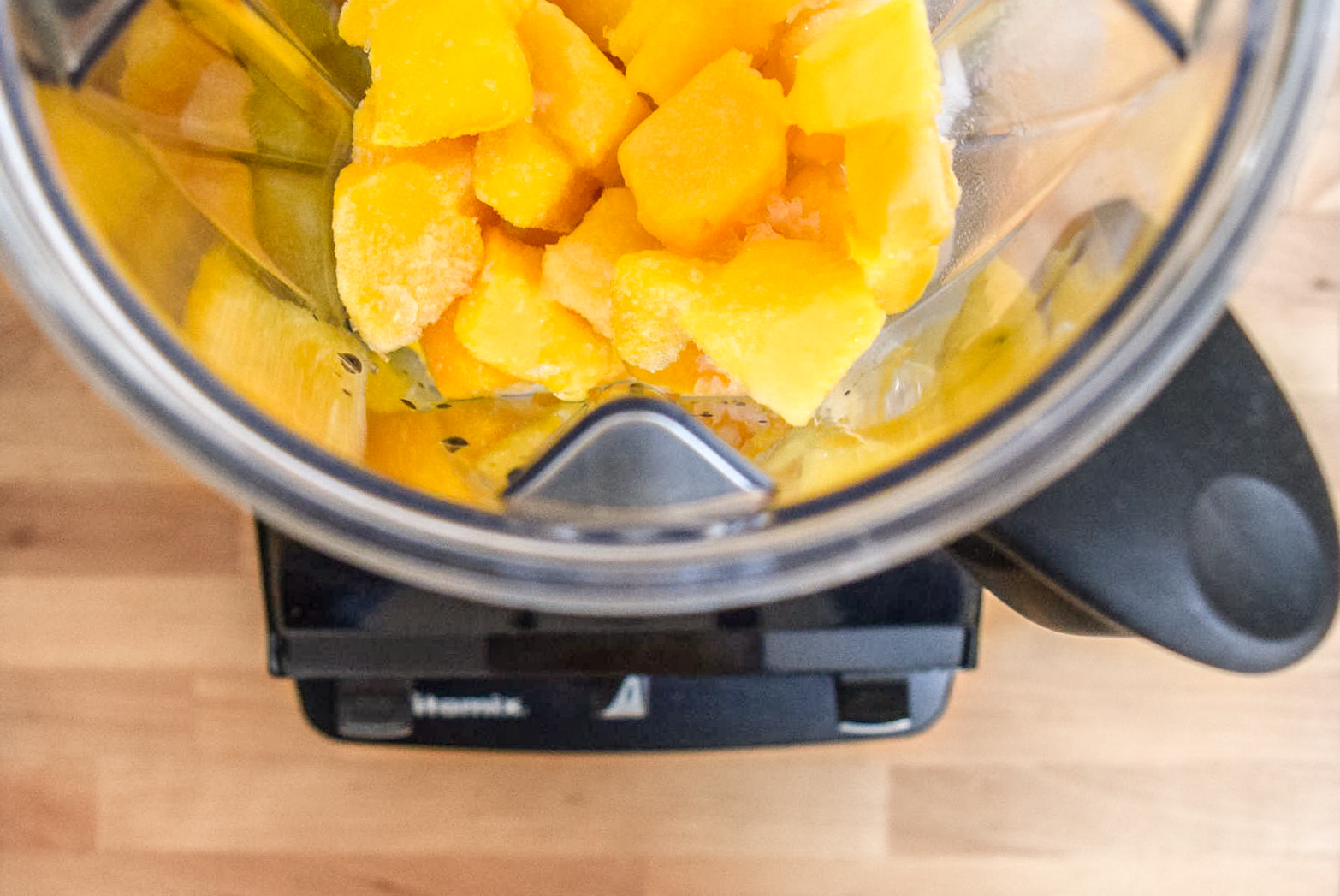 Frozen mango pieces and almond milk in Vitamix blender from top for Two-Ingredient Almond Mango Ice Cream